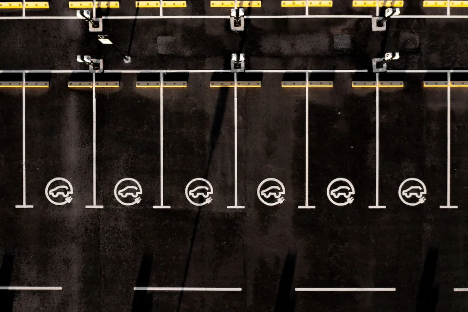 Overhead view of black asphalt parking lot with white lined parking spots with EV charging logos.